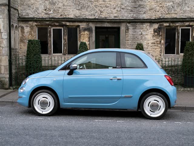 Lyseblå Fiat 500 parkeret foran et stenhus